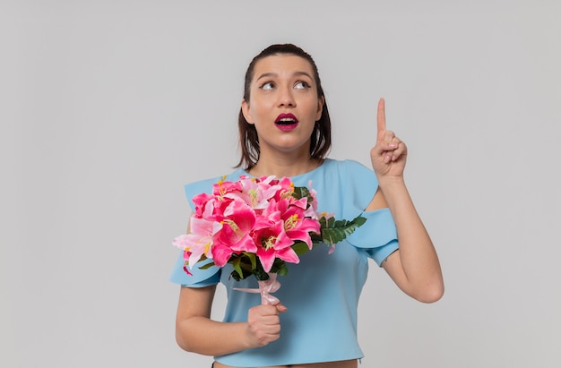 Mujer joven y bonita sorprendida sosteniendo un ramo de flores mirando y apuntando hacia arriba