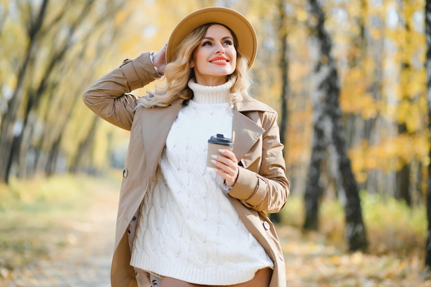 Mujer joven y bonita con taza de café en el parque de otoño