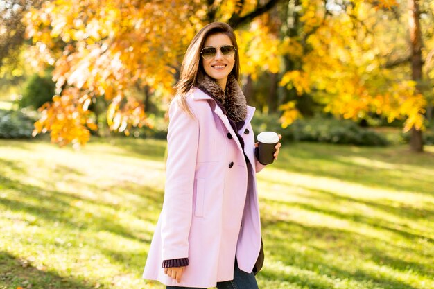 Mujer joven y bonita con taza de café en el parque de otoño