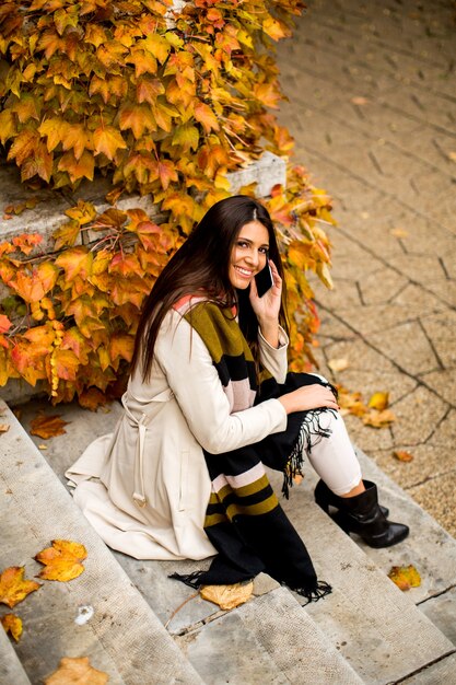 Mujer joven y bonita con teléfono móvil en el parque de otoño