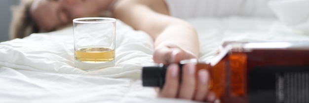 Mujer joven borracha yace en la cama en una botella de alcohol