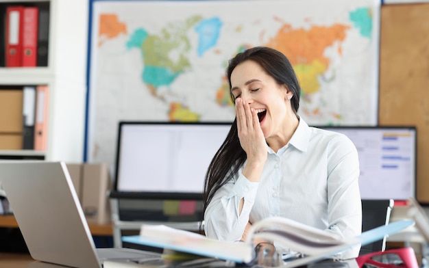 Mujer joven bosteza en el lugar de trabajo para portátil