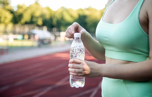 Una mujer joven con una botella de agua entrenando en el estadio