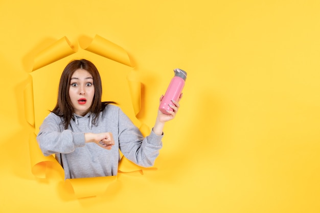 Mujer joven con botella rosa sobre papel amarillo atleta de gimnasio de fondo en forma interior