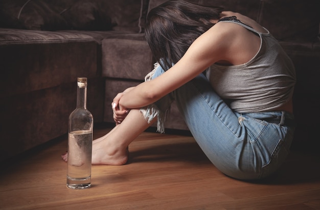 Mujer joven con una botella de vodka en casa.