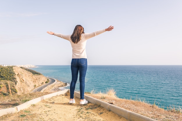 Mujer joven con los brazos abiertos mirando el mar