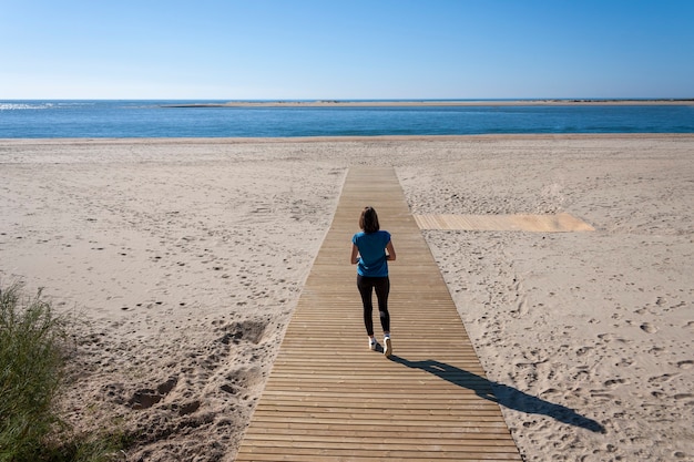 Mujer joven con los brazos extendidos caminando por la pasarela de la playa