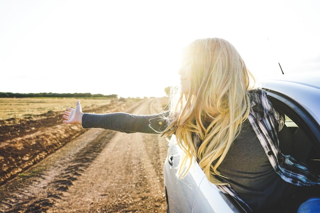 Foto mujer joven con los brazos extendidos inclinándose desde la ventana del coche contra el cielo despejado