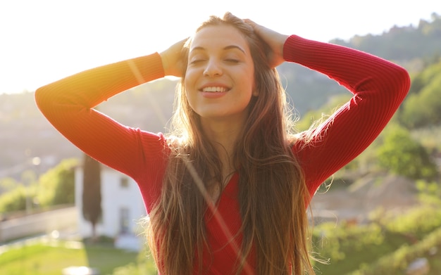 Mujer joven con los brazos levantados disfrutando de la brisa primaveral en el parque