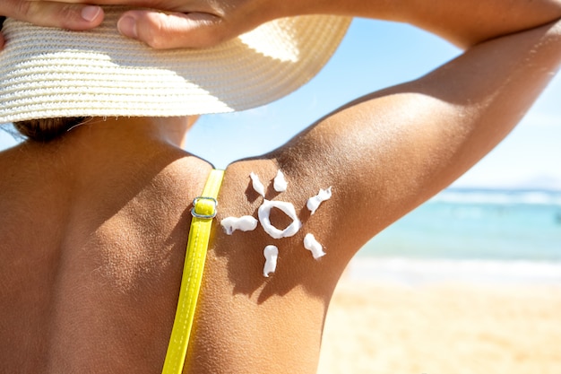 Foto mujer joven broncearse en la playa con protector solar en forma de sol en su hombro