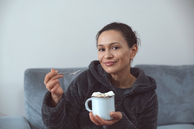 mujer joven de buen humor con un cordón de chocolate caliente con malvaviscos mirando a la cámara.