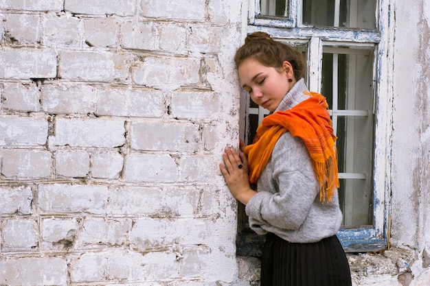 Mujer joven con bufanda naranja en la vieja pared de ladrillos blancos como fondo
