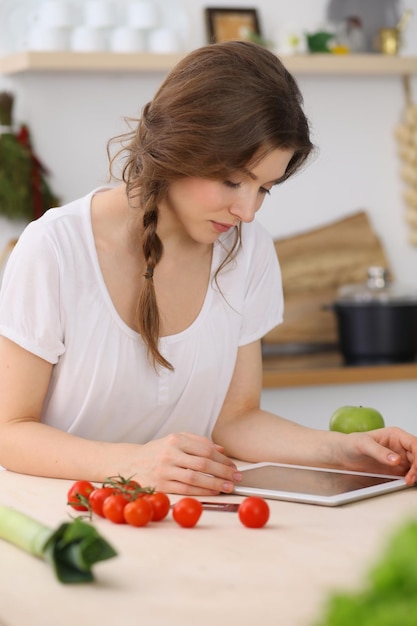 Mujer joven en busca de una nueva receta para cocinar en una cocina. El ama de casa está haciendo compras en línea con una tableta y una tarjeta de crédito.