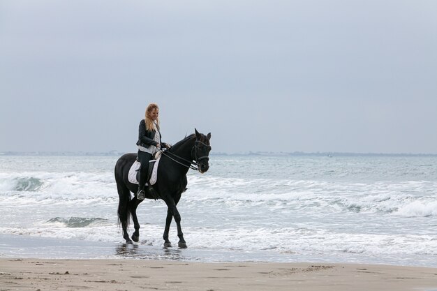 Mujer joven a caballo en la playa en un día nublado