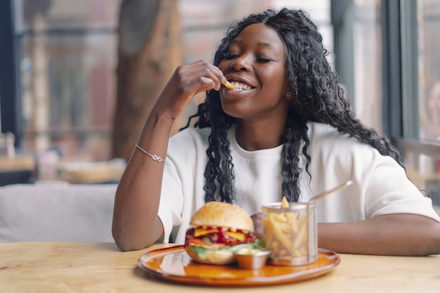 Mujer joven con cabello afro comiendo una sabrosa hamburguesa clásica con papas fritas