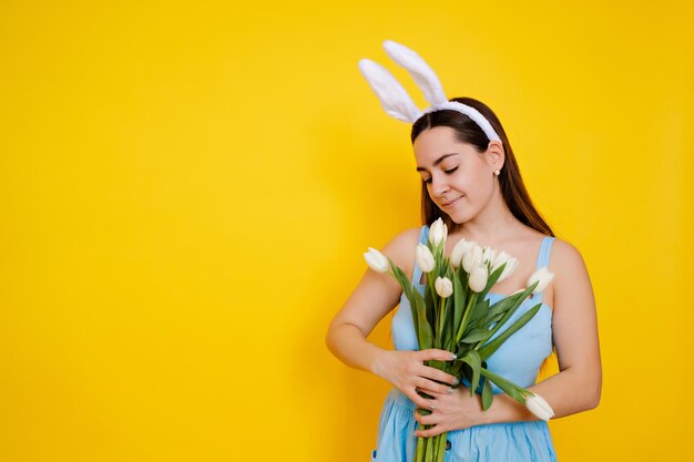 mujer joven de cabello castaño con orejas de conejo el día de Pascua sosteniendo flores tulipanes blancos en ella