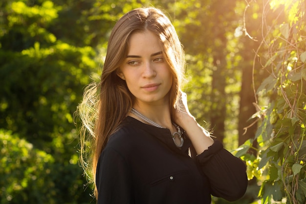 Mujer joven con cabello largo en blusa negra y collar de plata en el fondo de árboles verdes