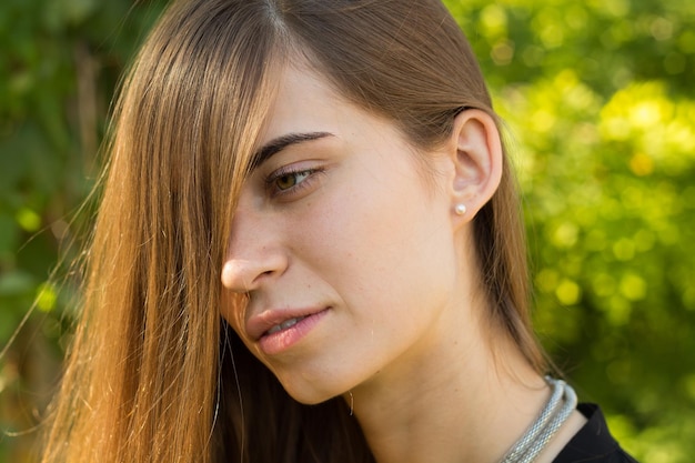 Mujer joven con cabello largo en blusa negra y collar de plata en el fondo de árboles verdes