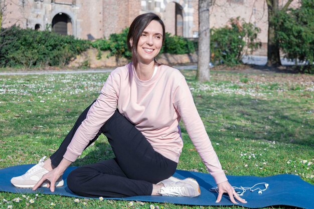 Mujer joven con cabello largo haciendo yoga en la alfombra en el parque de la ciudad. Prácticas de respiración y salud mental