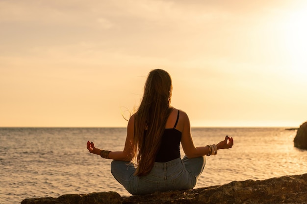 Mujer joven con cabello largo en traje de baño negro y braclets estilo boho practicando al aire libre en estera de yoga