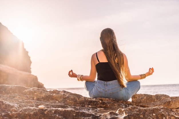 Mujer joven con cabello largo en traje de baño negro y braclets estilo boho practicando al aire libre en estera de yoga