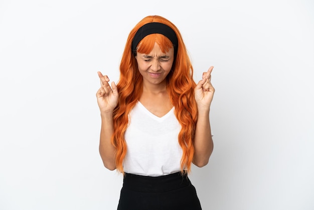 Mujer joven con cabello naranja aislado sobre fondo blanco con los dedos cruzados