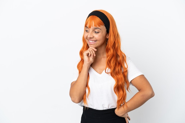 Mujer joven con cabello naranja aislado sobre fondo blanco mirando hacia un lado y sonriendo