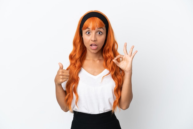 Mujer joven con cabello naranja aislado sobre fondo blanco que muestra el signo de ok y el pulgar hacia arriba gesto