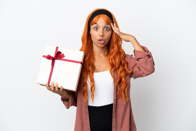 Mujer joven con cabello naranja sosteniendo un regalo aislado sobre fondo blanco con expresión de sorpresa