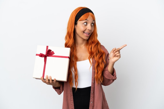 Mujer joven con cabello naranja sosteniendo un regalo aislado sobre fondo blanco con la intención de darse cuenta de la solución mientras levanta un dedo hacia arriba