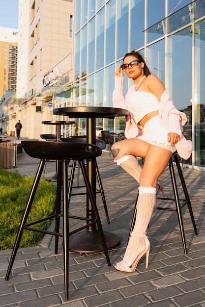 Mujer joven con cabello ondulado posando al aire libre en una calle de la ciudad con gafas de sol