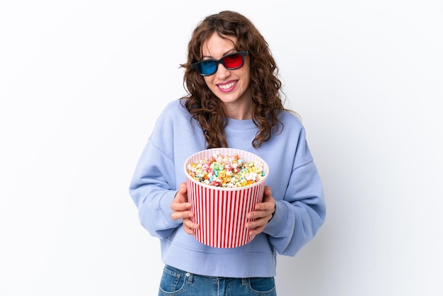 Mujer joven con cabello rizado aislado sobre fondo blanco con gafas 3d y sosteniendo un gran cubo de palomitas de maíz