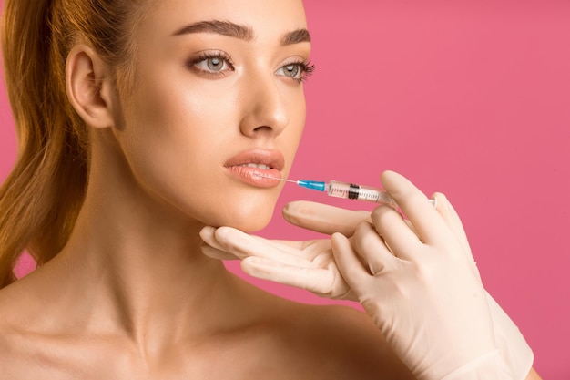 Una mujer joven de cabello rojo largo está recibiendo inyecciones en los labios de un profesional médico que lleva