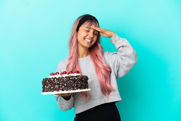 Mujer joven con cabello rosado sosteniendo pastel de cumpleaños aislado sobre fondo azul sonriendo mucho