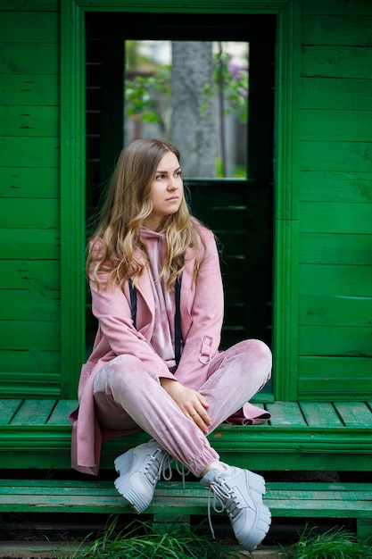 Una mujer joven con cabello rubio de apariencia europea se sienta en los escalones. Chica en un traje rosa y zapatillas
