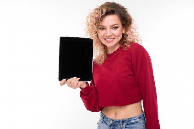 Mujer joven con cabello rubio rizado sostiene una tableta y sonríe