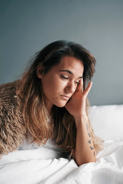 Foto mujer joven con la cabeza en las manos sentada en la cama en casa