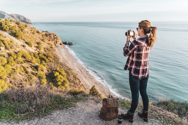 Mujer joven de la cadera con una mochila explorar y fotografiar la costa en un hermoso día. Concepto de exploración y aventuras.