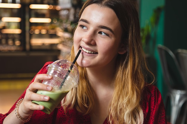 Una mujer joven en un café bebe un café con leche verde