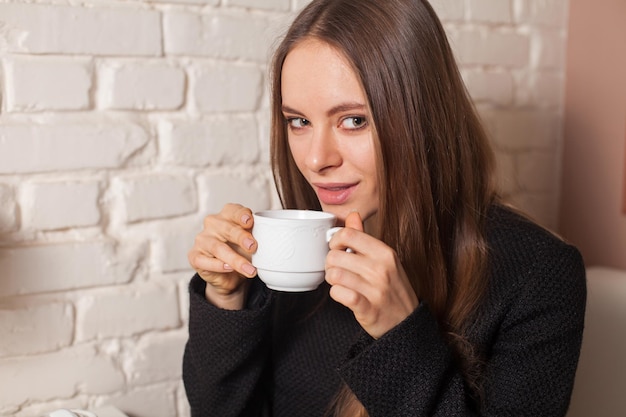 Mujer joven en café bebiendo aquí té de bebida favorita en taza blanca