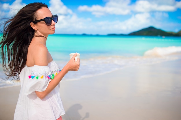 Mujer joven con café caliente disfrutando de la vista de la playa