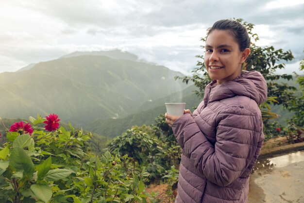 Foto mujer joven con un café caliente con hermosos paisajes montañosos colombianos