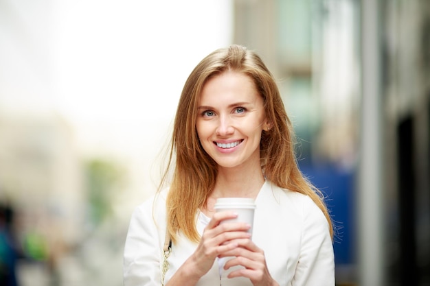 Mujer joven con café para llevar en la calle. Fondo desenfocado.