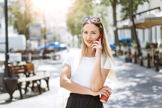 Mujer joven con un café para llevar hablando por un teléfono inteligente