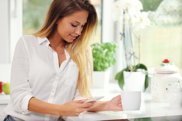 mujer joven, con, café, y, smartphone, en, cocina