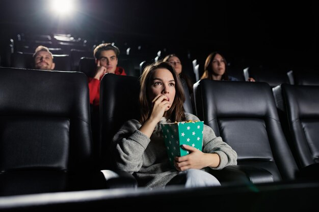 Mujer joven con una caja de palomitas de maíz en el estreno de la película Sala de cine cómoda y elegante