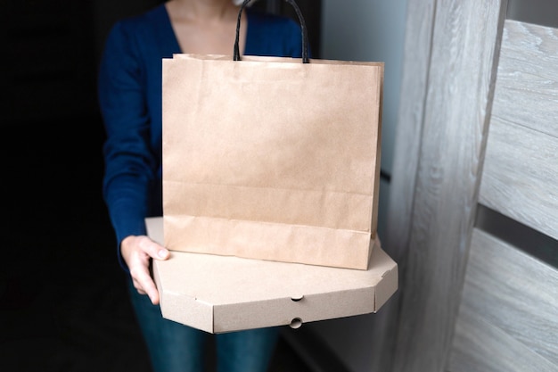 Mujer joven con caja de pizza de cartón en blanco y bolsa de papel.