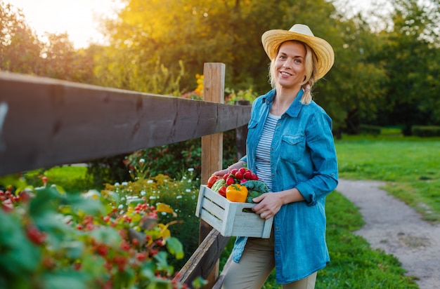 Mujer joven con caja de verduras ecológicas frescas al atardecer