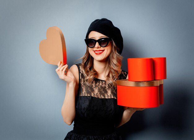 Mujer joven con cajas de regalo en la pared gris