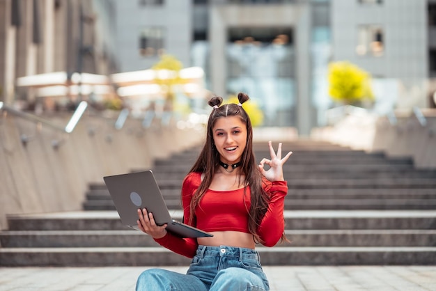 Mujer joven en la calle usando laptop y muestra ok